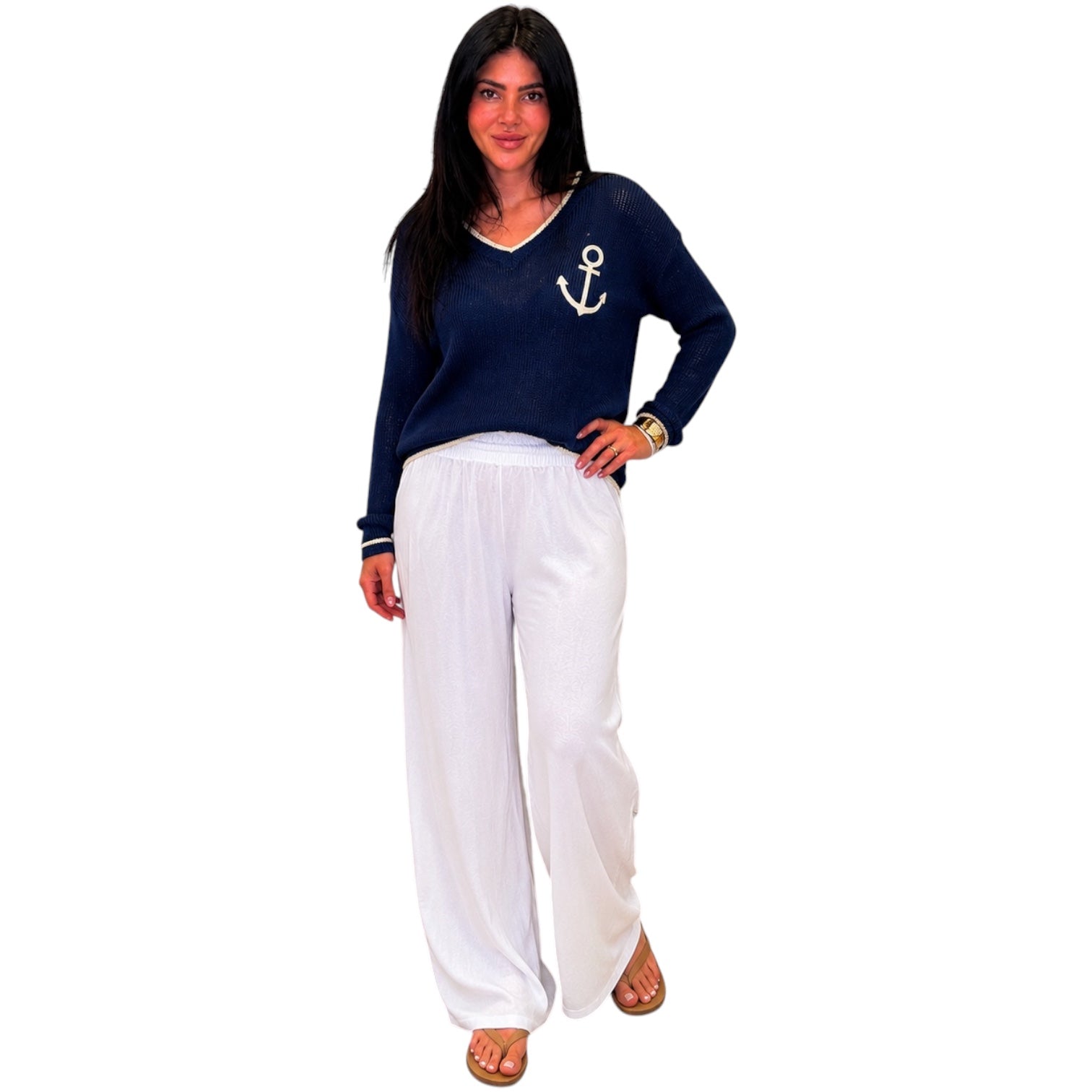 Woman wearing a navy sweater with an anchor design and white pants on a white background