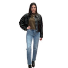 Woman wearing a black leather jacket, olive shirt, and blue jeans on a white background