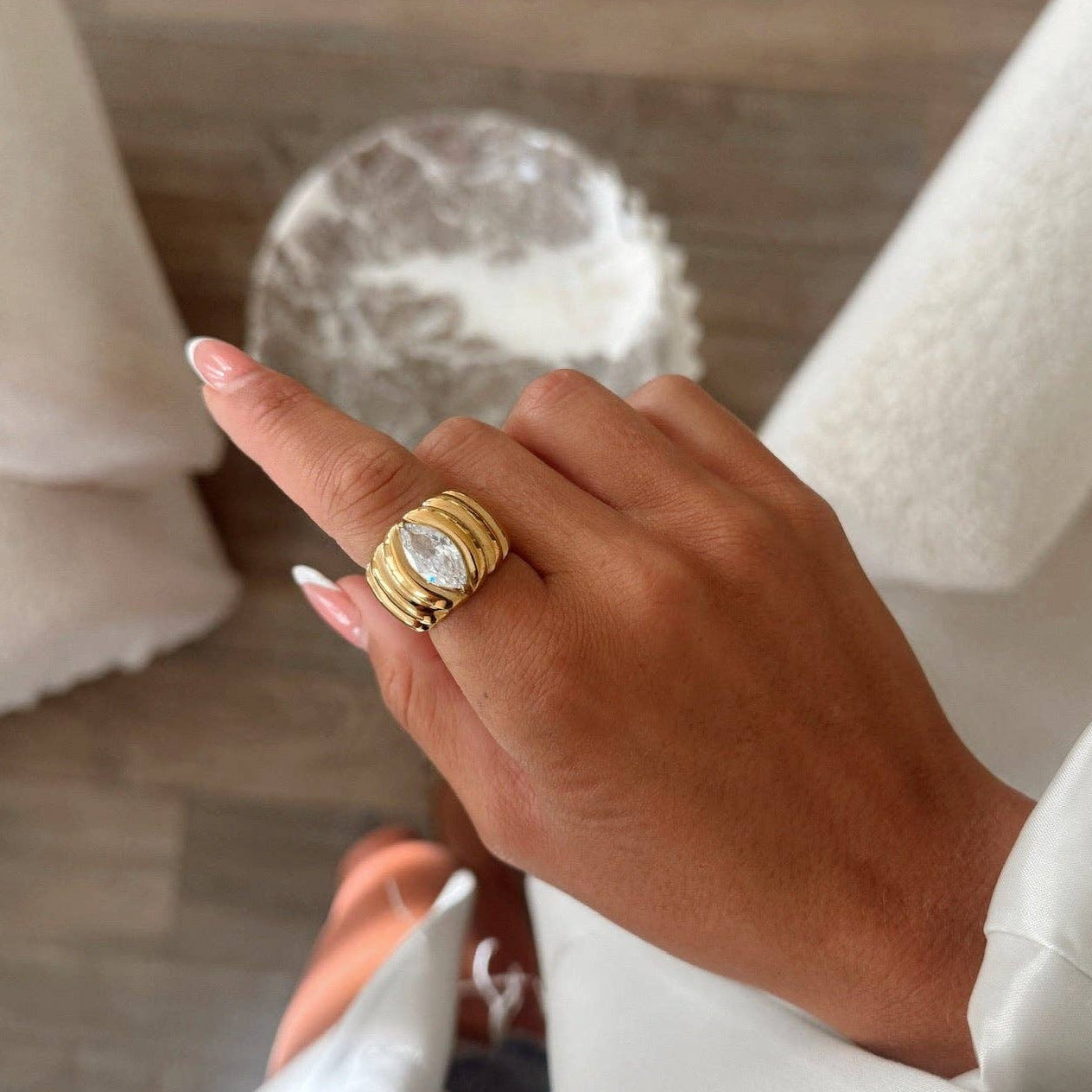 Hand wearing a gold ring with a clear stone, blurred background