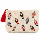 An off-white sherpa zip pouch decorated with embroidered nutcracker figures in red, blue, green, and pink, featuring a red tassel zipper pull on a white background.