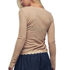 Woman wearing a beige long-sleeve top with lace trim on a white background