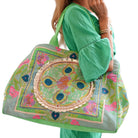 Person holding a decorative handbag with intricate patterns on a white background