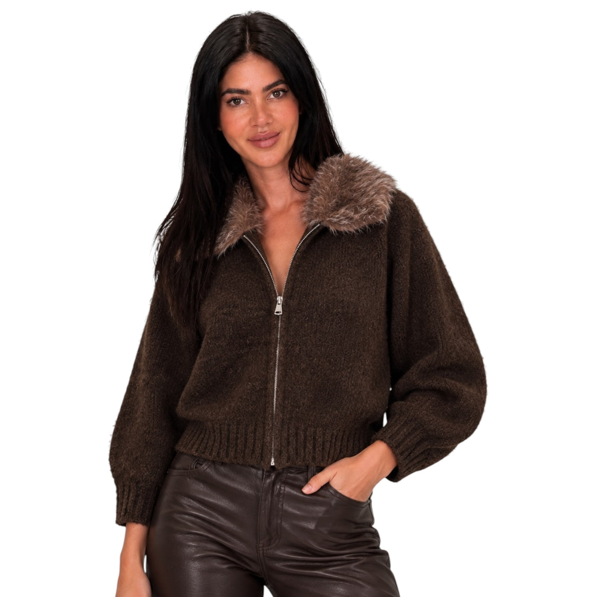 A woman modeling a dark brown knit zip-up jacket with a fuzzy brown faux-fur collar, paired with dark brown faux-leather pants, against a solid white background.