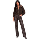 A woman modeling a dark brown knit zip-up jacket with a brown faux-fur collar, paired with dark brown faux-leather pants and black heels, against a solid white background.