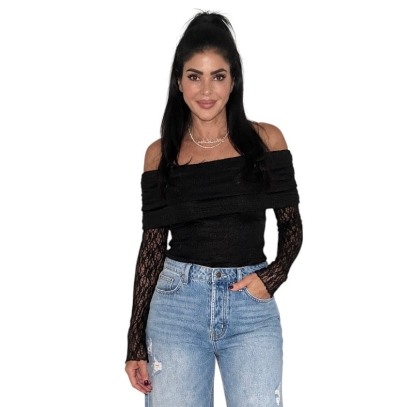A woman modeling a black off-the-shoulder knit bodysuit with sheer black lace long sleeves, paired with light-wash blue jeans, against a plain white background.