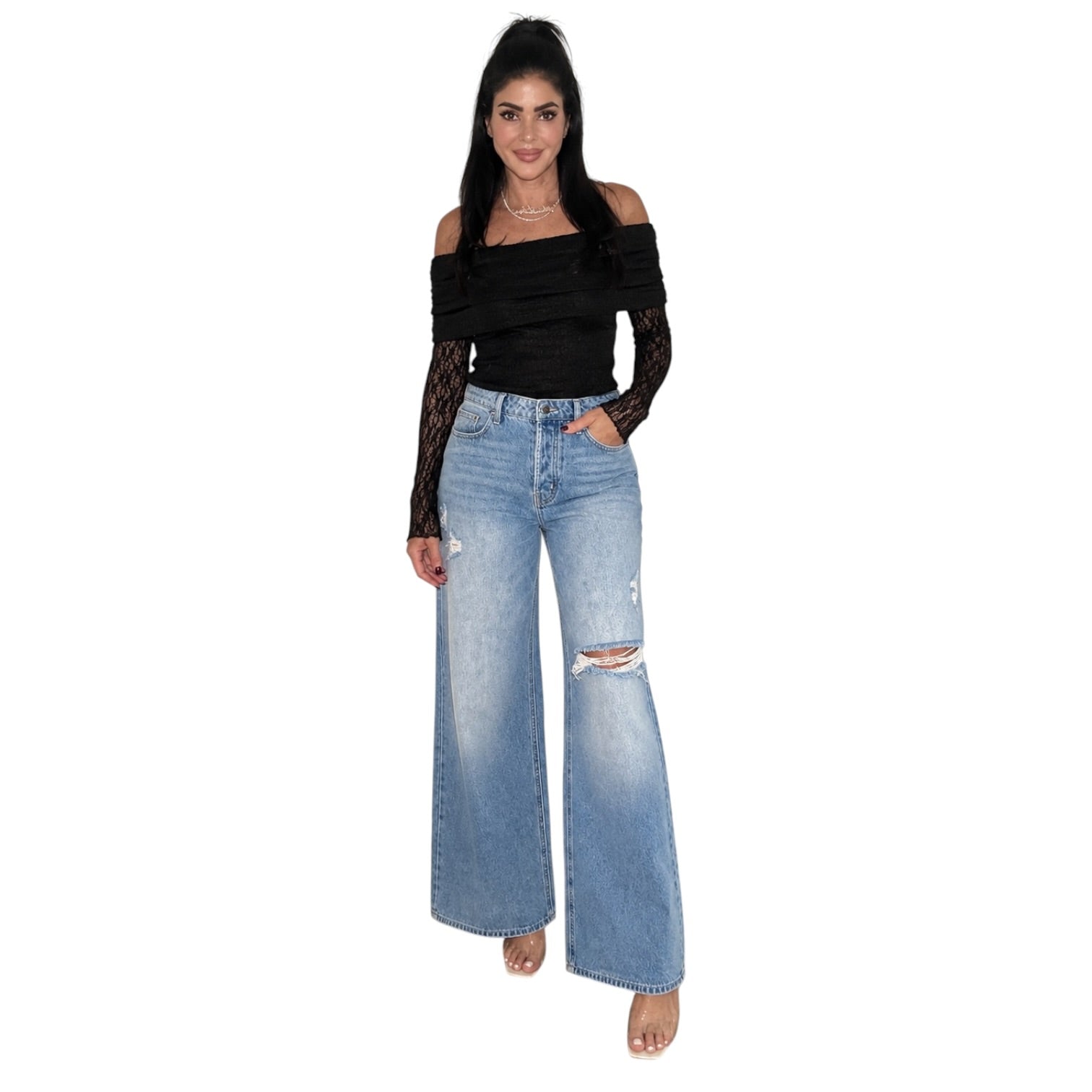 A woman modeling a black off-the-shoulder long-sleeve bodysuit with lace sleeves and light-wash blue wide-leg distressed jeans, shown against a plain white background.