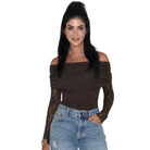 A woman modeling a dark brown off-the-shoulder knit bodysuit with long lace sleeves, paired with light blue jeans, against a plain white background.