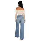 A woman shown from the back wearing a cream off-the-shoulder knit top with sheer long sleeves and light-wash blue wide-leg jeans, against a plain white background.