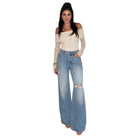 A woman modeling a cream off-the-shoulder knit top with long lace sleeves and light-wash blue wide-leg distressed jeans, shown against a plain white background.