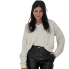 Woman wearing a cream sweater and black pants on a white background