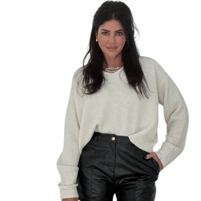 Woman wearing a cream sweater and black pants on a white background