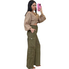 Woman taking a selfie wearing a beige cropped top and olive green cargo pants on a white background