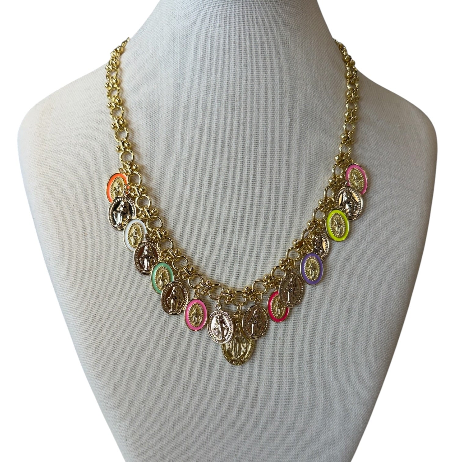 A gold-tone multi-strand necklace with small oval religious medallions in assorted colors, displayed on a light beige fabric mannequin bust against a white background.