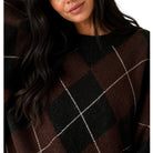 Close-up of a woman wearing a dark brown and black argyle sweater with thin white diagonal stripes, against a plain white background.