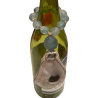 A beaded necklace with light blue-green round beads and a large natural oyster shell pendant, draped over a green glass bottle against a white background.