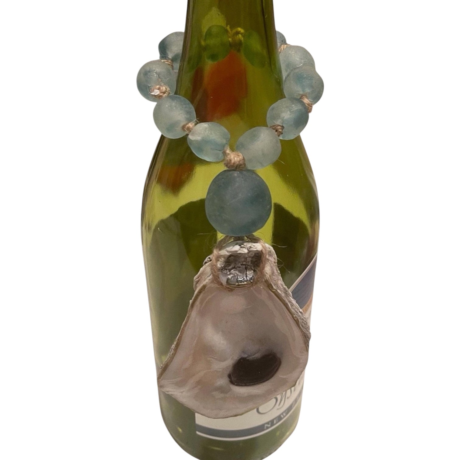 A beaded necklace with light blue-green round beads and a large natural oyster shell pendant, draped over a green glass bottle against a white background.