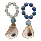 Two beaded drop earrings on a white background. One earring features light blue beads, a larger light blue bead, and a natural oyster shell pendant with gold trim.