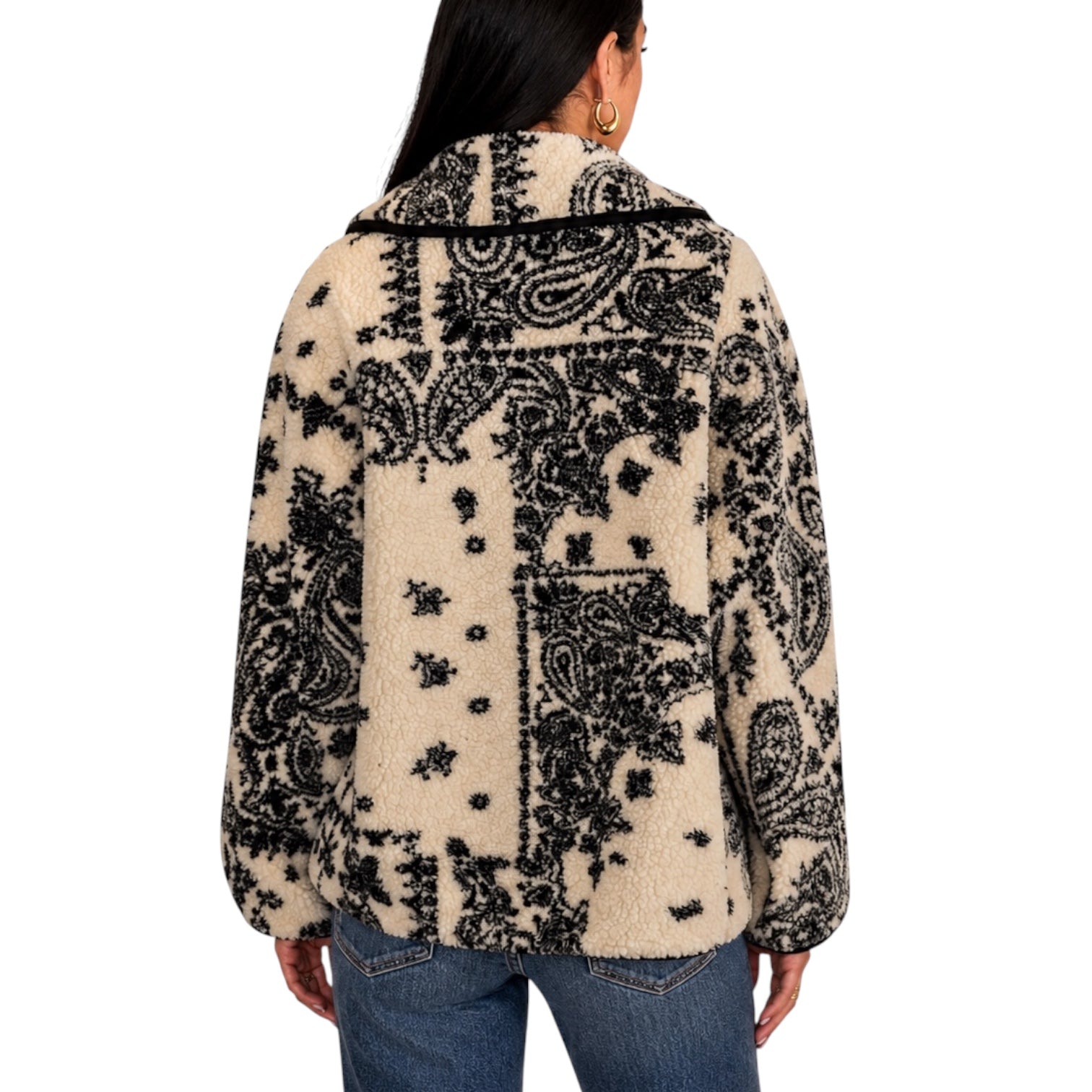 A woman viewed from the back wearing a sherpa fleece jacket with a black and cream paisley patchwork pattern, paired with blue jeans against a plain white background.