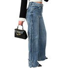 Person wearing blue jeans holding a black handbag on a white background