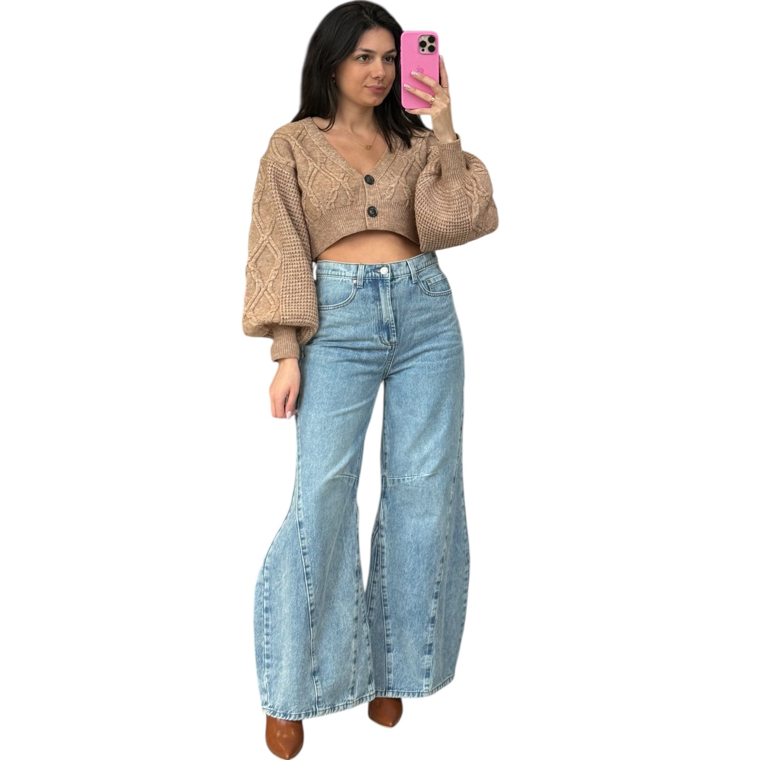 Woman taking a selfie wearing a beige cropped sweater and blue jeans on a white background