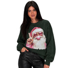 A woman modeling a dark forest green crewneck sweatshirt featuring a graphic print of a Santa Claus character wearing pink sunglasses and making a peace sign. She is also wearing black leather pants against a solid white background.