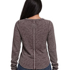 A woman viewed from the back wearing a long-sleeve waffle-knit top in a dark taupe-brown color, featuring a central seam and a square patch detail on the upper back.