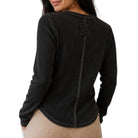 A woman wearing a black waffle-knit long-sleeve top, shown from the back against a plain white background.