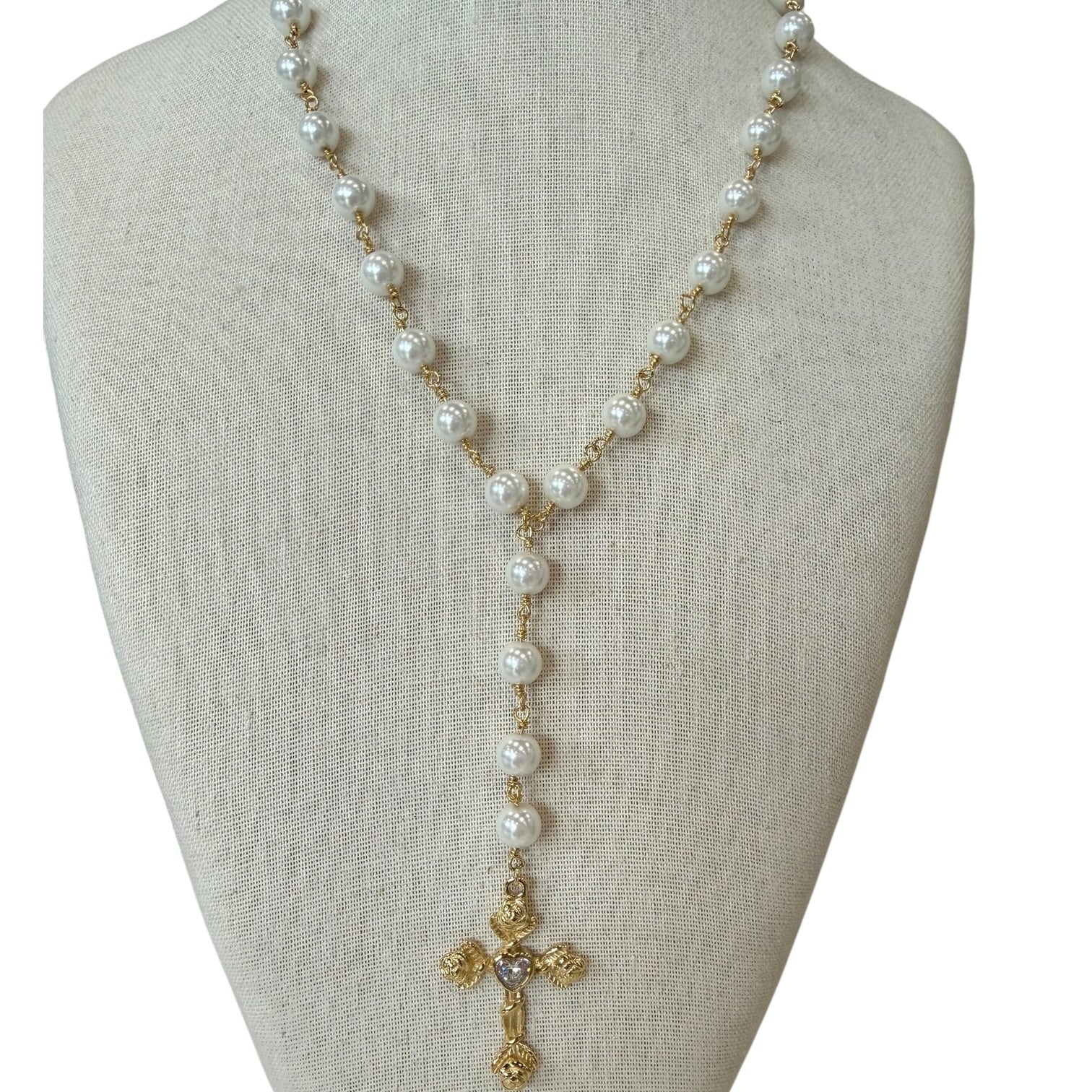 A gold and white pearl necklace displayed on a beige fabric jewelry bust against a white background.