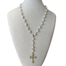 A long pearl rosary-style necklace with gold-tone chain links and a gold cross pendant, displayed on a cream fabric jewelry bust against a white background.