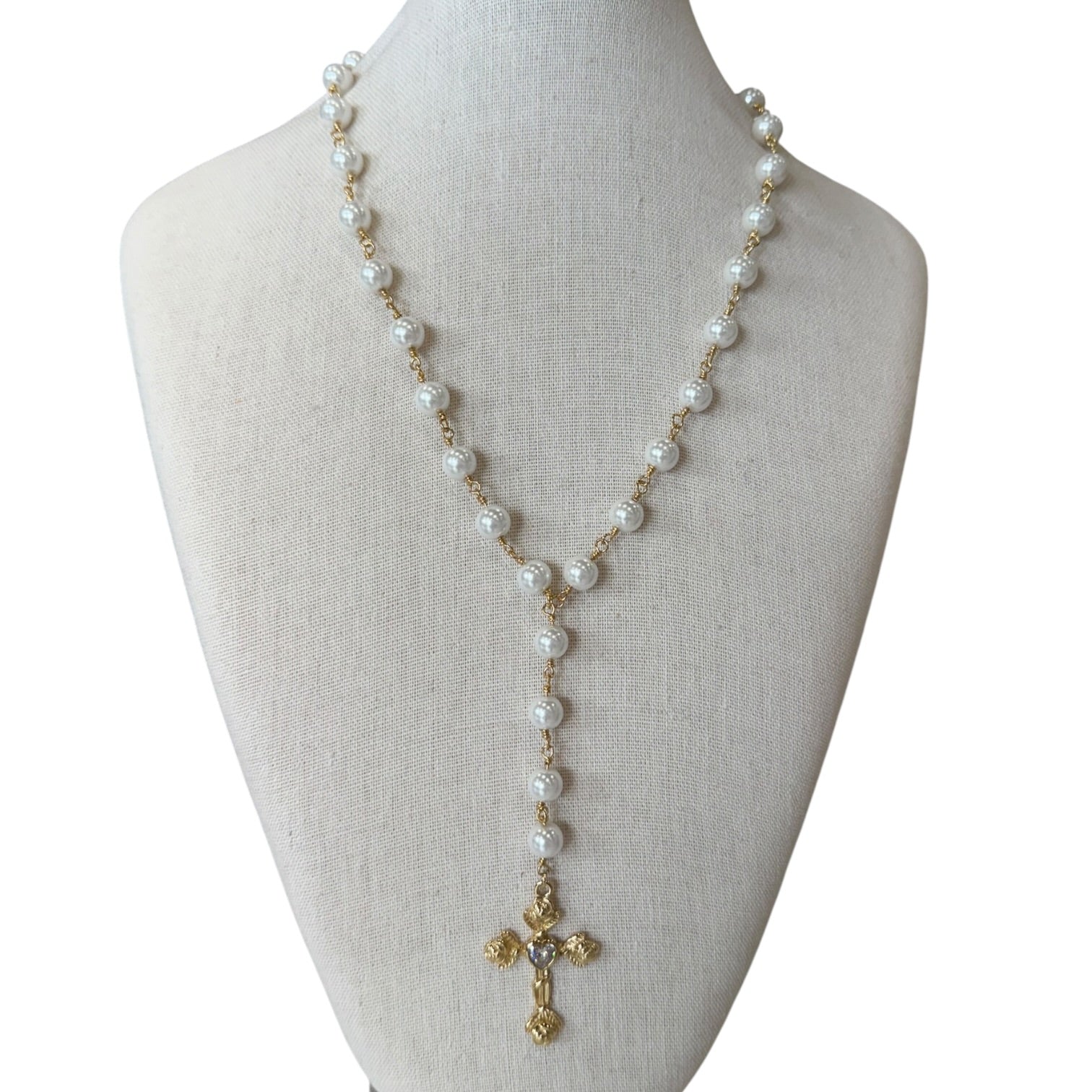 A long pearl rosary-style necklace with gold-tone chain links and a gold cross pendant, displayed on a cream fabric jewelry bust against a white background.