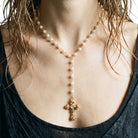 A close-up of a model wearing a gold and pearl Y-necklace with a cross pendant.
