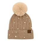 A beige ribbed knit pom-pom beanie with white faux-pearl embellishments and a small brown leather patch on the cuff, shown against a plain white background.
