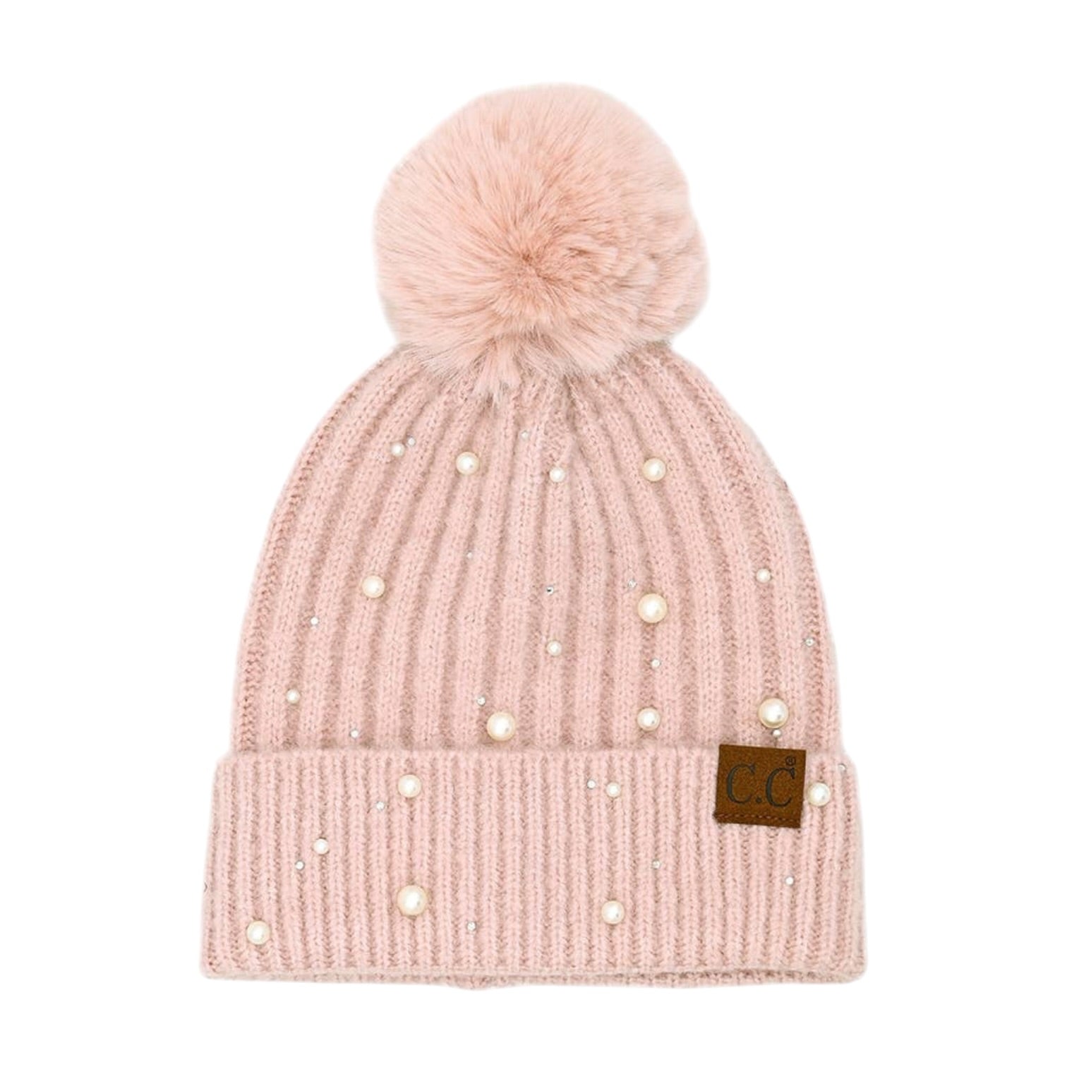 A light pink ribbed knit beanie hat with a fluffy pom-pom on top, decorated with scattered faux pearls and small rhinestones, featuring a brown leather patch with 'CG' on the folded cuff.