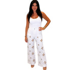 Woman wearing a white tank top and white pants with floral patterns on a white background