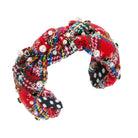 A handmade braided headband made from colorful patterned fabrics, decorated with white faux pearls and small black beads, shown on a plain white background.