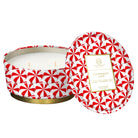A round wax candle in a patterned tin with its lid leaning against the open container. The tin has a red and white candy cane motif and a gold band at the base.