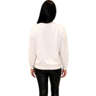 A woman viewed from behind wearing a plain white crewneck sweatshirt and black pants, set against a solid white background.