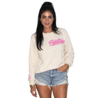 A woman modeling a cream-colored crewneck sweatshirt with a pink 'Pretty Beautiful' graphic on the chest, paired with light-wash denim shorts, against a solid white background.