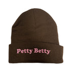 A dark brown knit beanie hat with a folded cuff, featuring the text 'Petty Betty' embroidered in pink on the front, set against a plain white background.