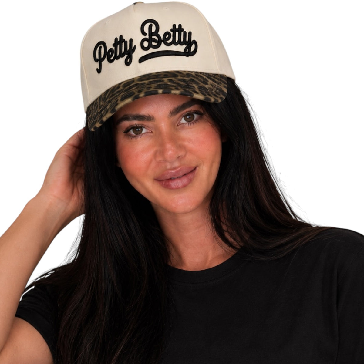 A woman wearing a cream-colored snapback cap with a leopard-print brim and 'Petty Betty' embroidered in black script on the front, paired with a black t-shirt against a solid white background.