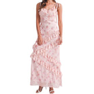 a woman wearing a pink floral dress with ruffles on white background