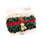 Scrunchie charm set featuring three ruffled scrunchies in green plaid, red, and cream satin, decorated with a gold teddy bear charm wearing a green bow and a small gold bell.