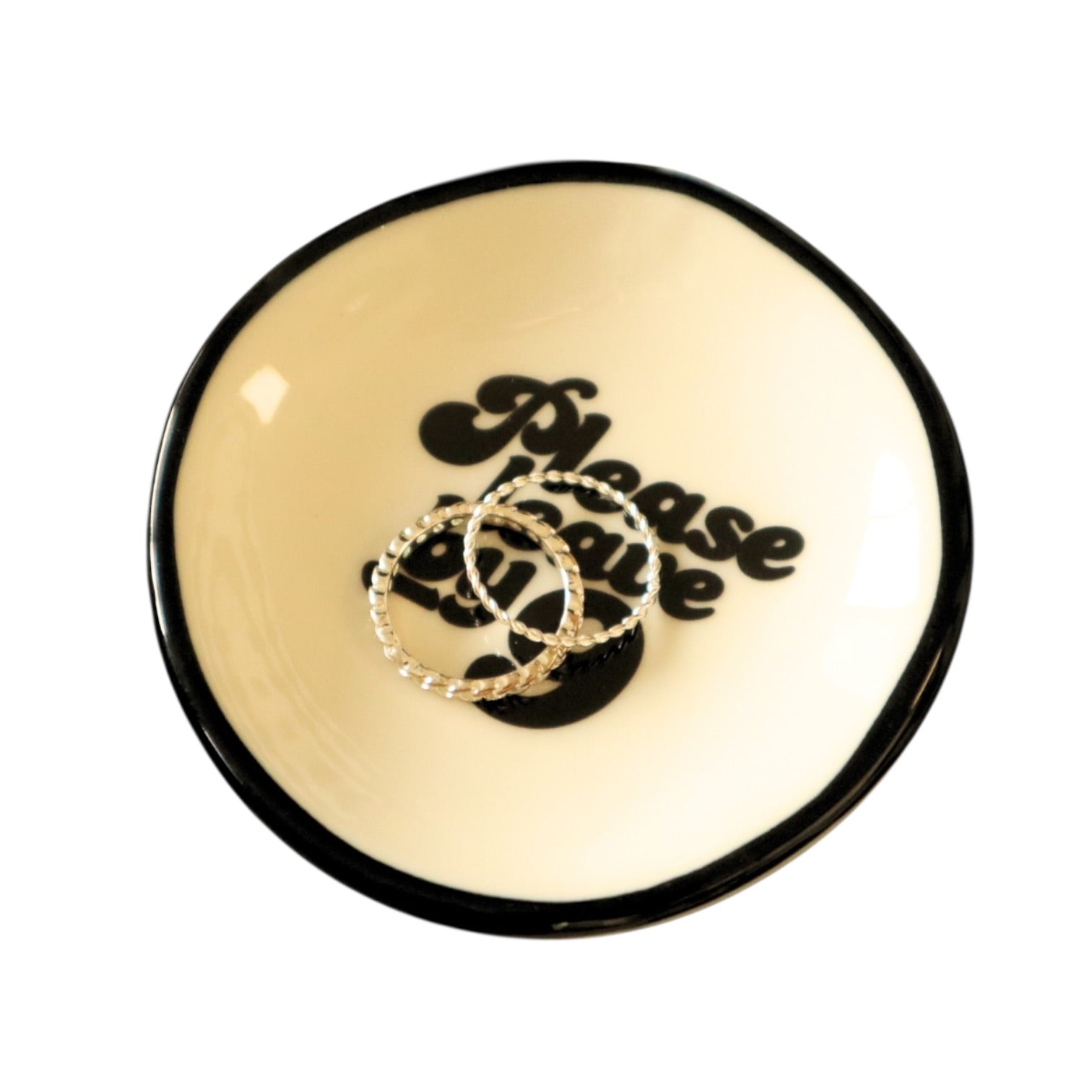 Round beige trinket dish with black rim and 'Please勿乱放' text, holding two rings.