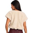 A woman shown from the back wearing a short-sleeve cream faux fur cropped top and burgundy faux leather pants, against a solid white background.