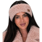 A woman wearing a fluffy light pink headband with a small tan leather patch that reads 'CC', shown against a plain white background.