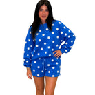 A woman modeling a matching blue and white polka dot lounge set, featuring a long-sleeve sweatshirt and drawstring shorts, against a plain white background.