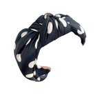Black headband with white polka dots held by a hand against a light background