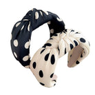 Two polka dot headbands, one black and white, one beige and black, held by a hand against a light background.