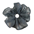 Black polka dot scrunchie held by a hand against a white background