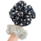 Black scrunchie with white polka dots held by a hand against a light background